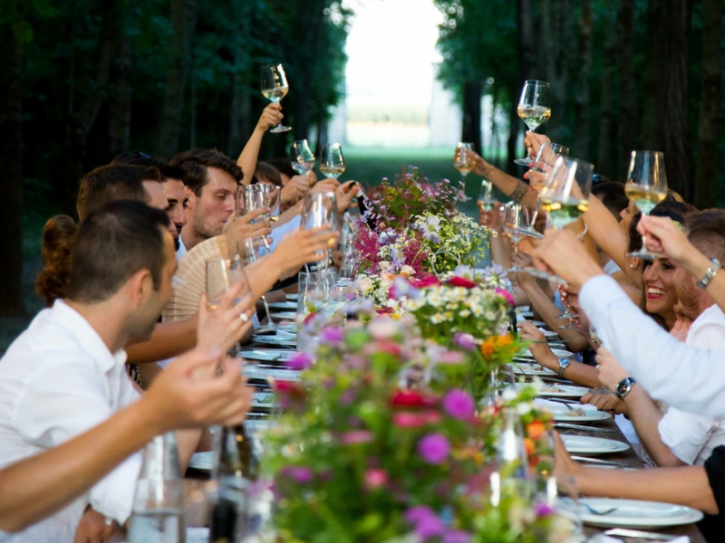 People gather around a table set with flowers at a wedding, raising a glass in a toast