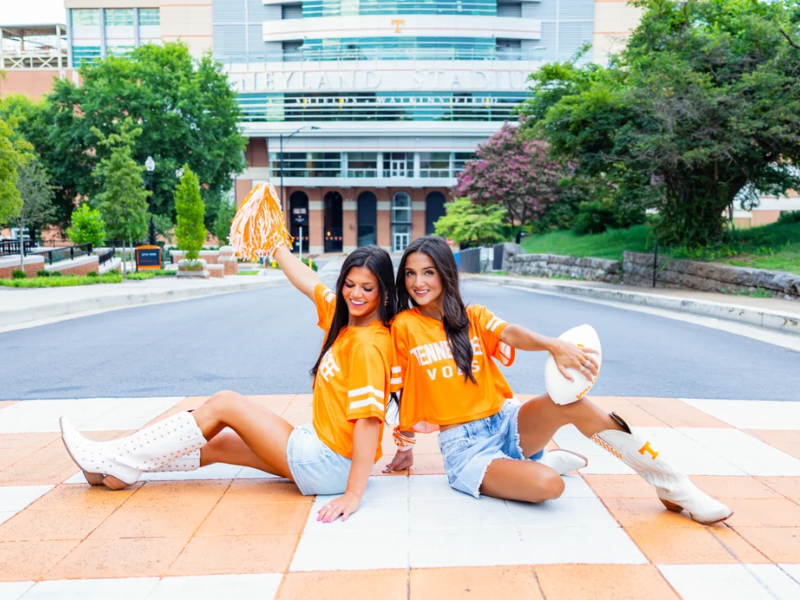two brunette girls wearing Tennessee jerseys sit back tob back smiling