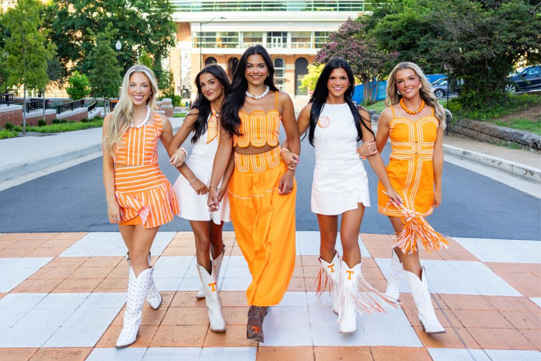 5 women smile at the camera wearing orange and white gameday outfits from Josie's